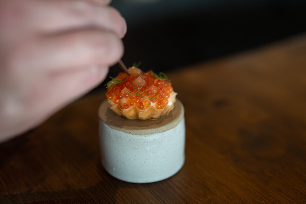 A hand finishing a small tartlet topped with orange roe