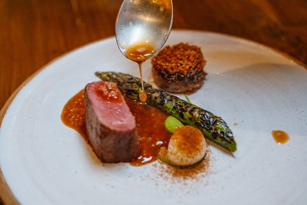 A sauce spooned over a pink-cooked cut of meat with charred asparagus
